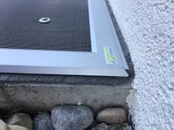 Eine Lichtschachtabdeckung liegt auf einen Betonsockel und dichtet mit Bürsten zur Wand und nach unten ab