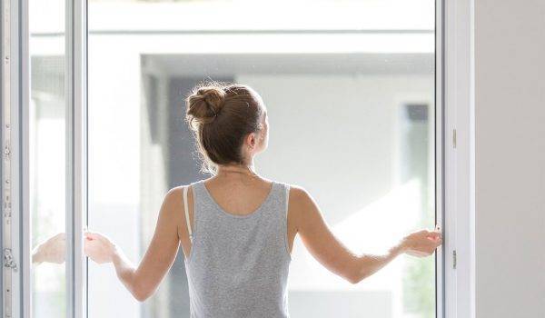 Frau steht innen am Fenster und hängt einen Fliegengitter Spannrahmen am Fenster ein
