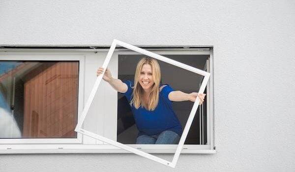 Frau mit Fliegengitterrahmen der am Fenster montiert wird