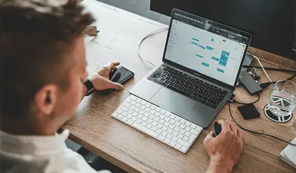 ein Mann, der mit einem Laptop und einem Telefon am Schreibtisch sitzt
