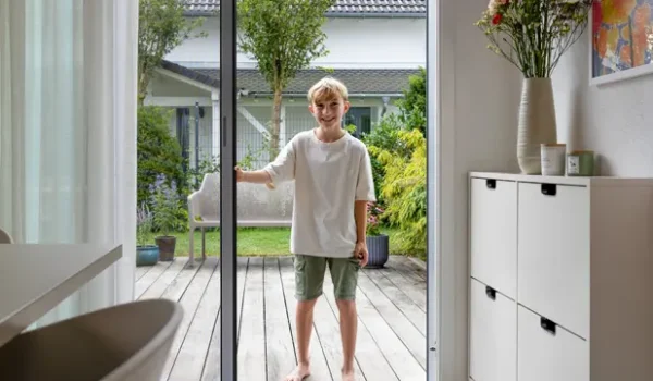 Kind öffnet Mückengitter Schiebeanlage an Terrassentür für insektenfreien Zugang